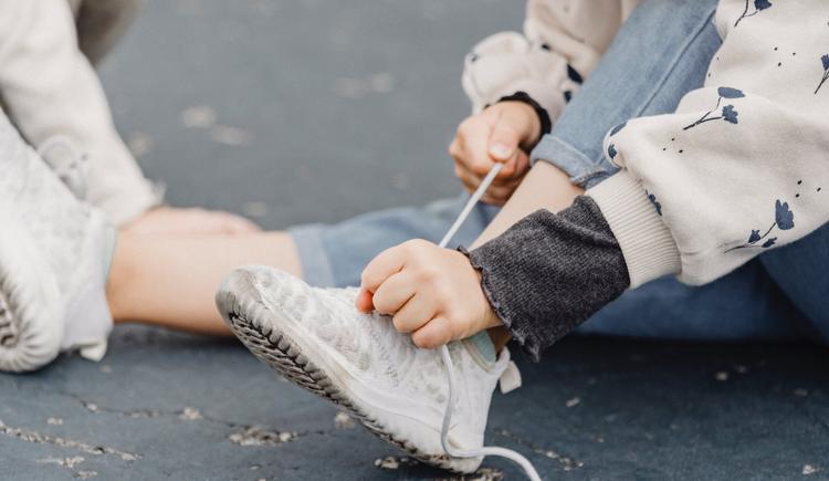 A child client makes use of their occupational therapy motor planning skills by tying their shoes, which was a motor planning goal and part of the occupational therapy activities their OT recommended.