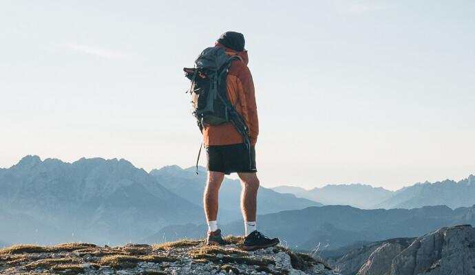 A person stands on a mountain wearing a backpack.