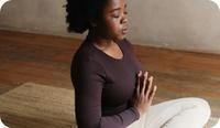 A woman sits cross legged with prayer hands to practice meditation and psychological flexibility.