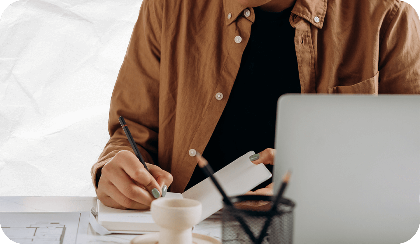 A therapist works on client session notes at their laptop and notebook while considering whether they are writing progress notes vs psychotherapy progress notes