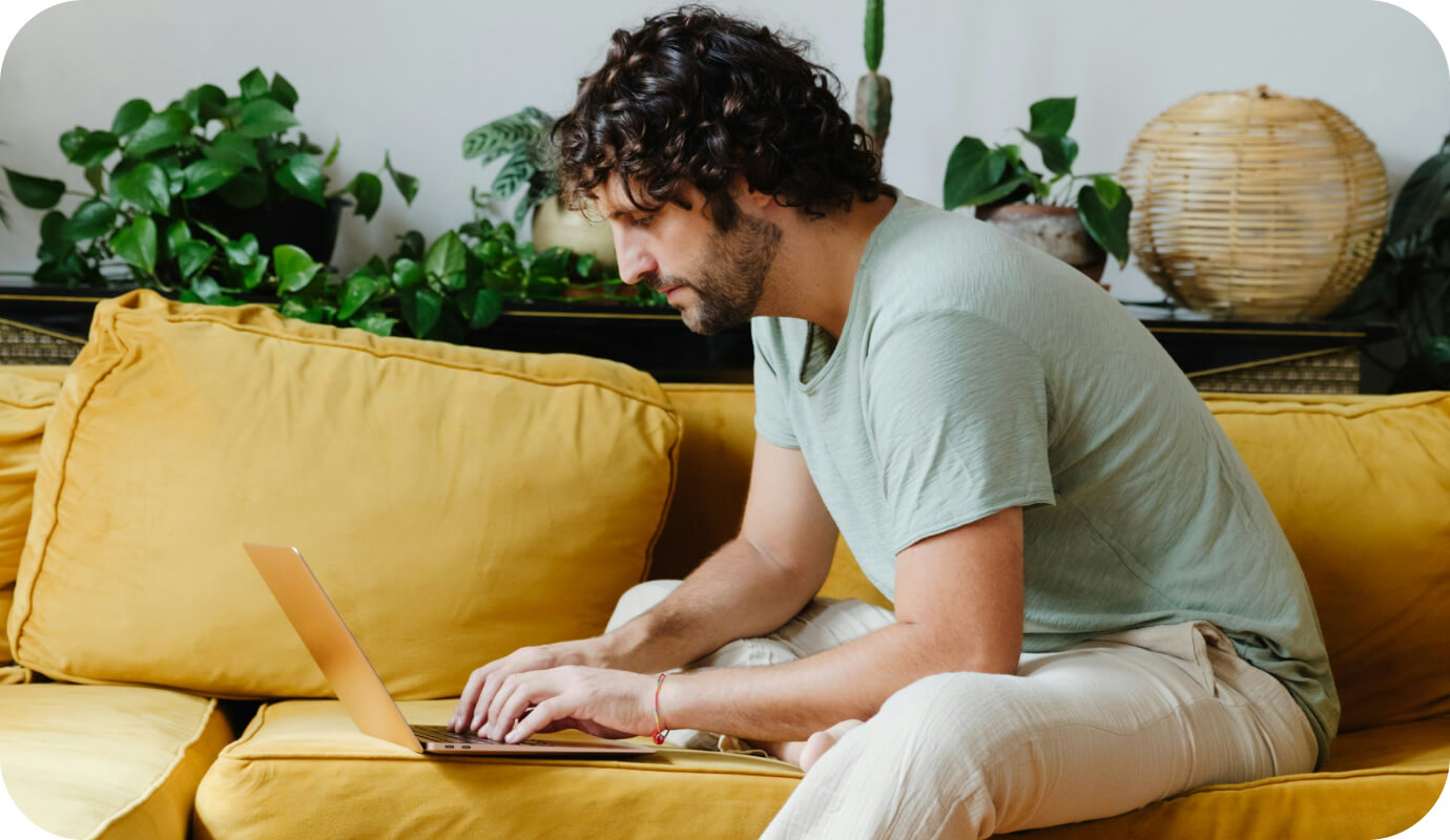 A male therapist sits on a yellow couch with his laptop and works on private practice marketing strategies