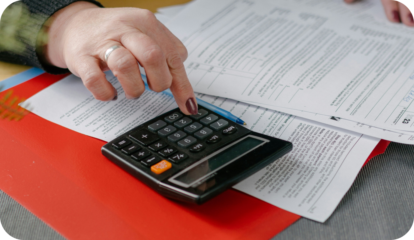 A therapist's hand types on the calculator on their desk while working on their tax forms on the desk